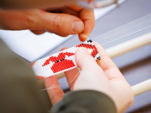 Close-up of hands beading a red and white pattern on a loom.