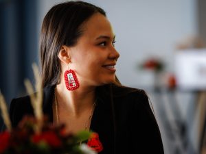 Close-up of a smiling attendee wearing red beaded earrings and a red dress pin during a REDress Day event.