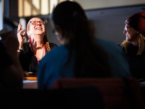 Two attendees laugh together at a table, sunlight highlighting their faces during the gathering.