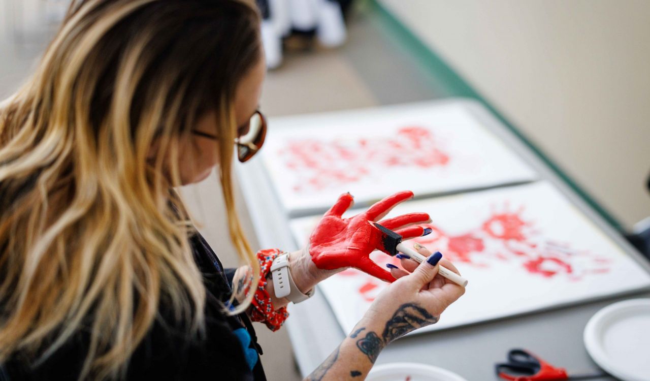 An attendee paints their palm red over a table covered with art supplies and paper.