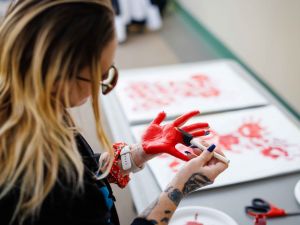 An attendee paints their palm red over a table covered with art supplies and paper.
