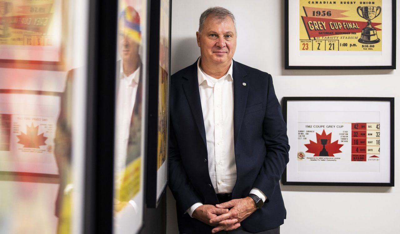 A man poses for a photo standing against a wall beside several framed images.