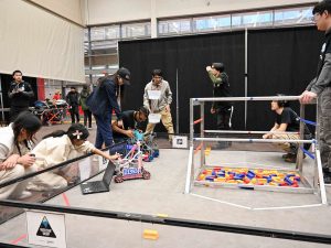 A group of students work on computers and with robots while preparing them to navigate a competition space with colourful blocks.