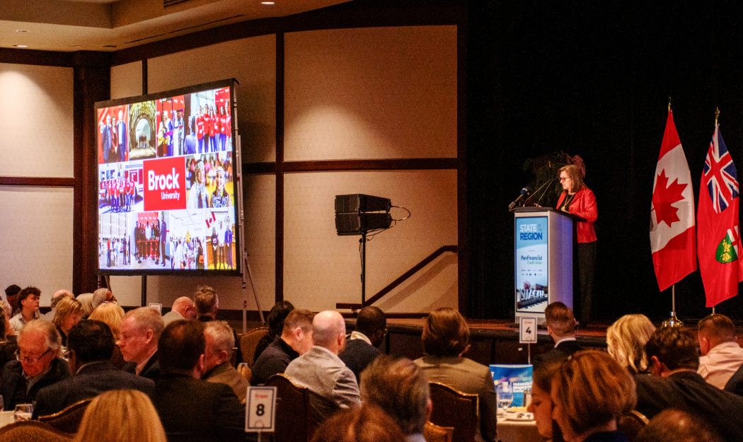 A woman speaks to an audience from behind a podium in a conference hall.