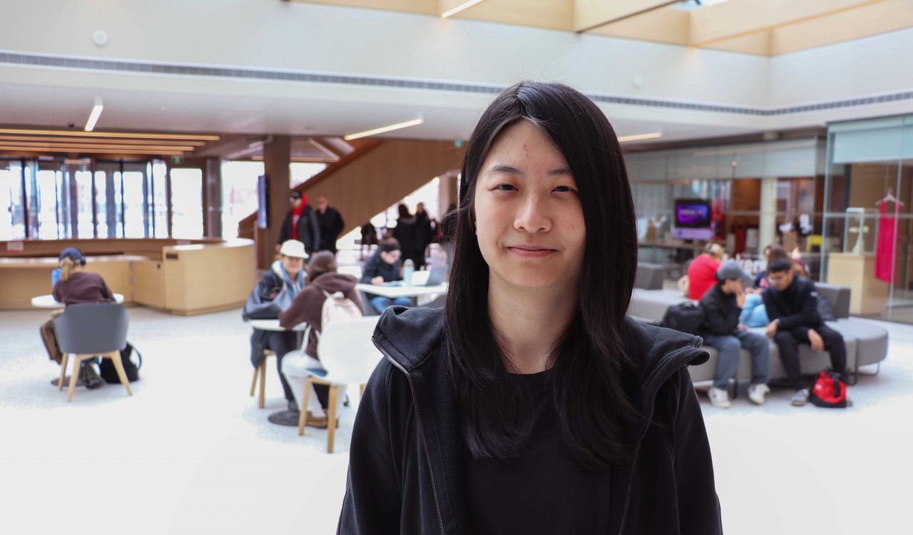 Portrait of computer Science student Jiani Zhao, with people sitting at tables and on chairs in the background.
