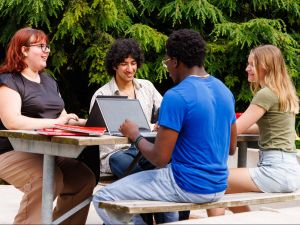 Four people sit at a picnic table talking to each other.