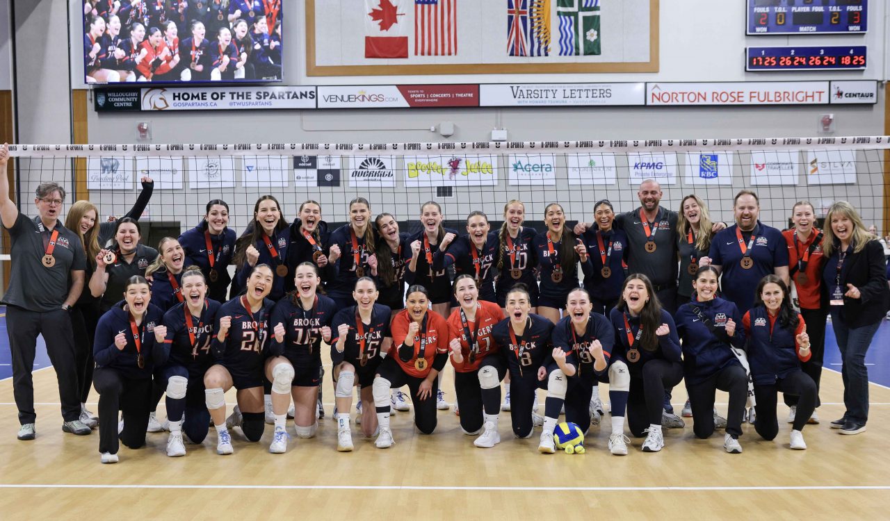 A large group of young women pose with bronze medals in a gymnasium.