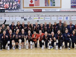 A large group of young women pose with bronze medals in a gymnasium.