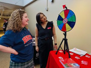 Two people look at a small spinner wheel with different prizes written on it.
