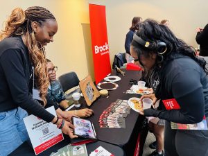 A high school student speaks to two university representatives at an information table.