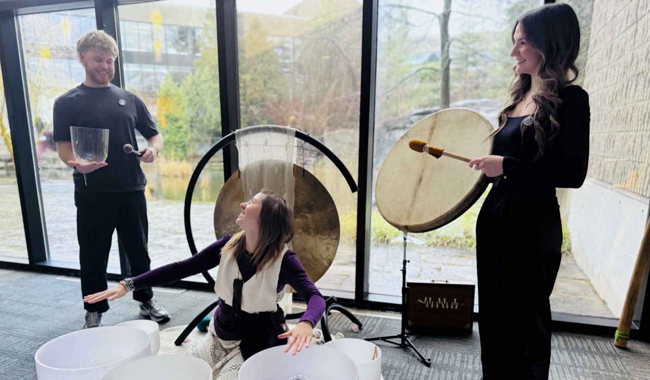 Three people play instruments an sound bowls in front of a window.