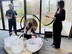 Three people play instruments an sound bowls in front of a window.
