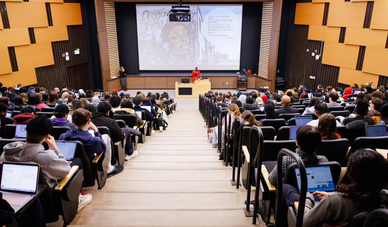 A woman speaks to an audience from the front of a full lecture hall.