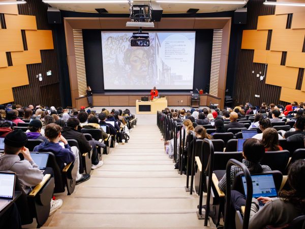 A woman speaks to an audience from the front of a full lecture hall.