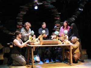 Group of people sit around a wooden table with stacks of books behind them.