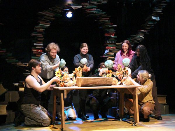 Group of people sit around a wooden table with stacks of books behind them.