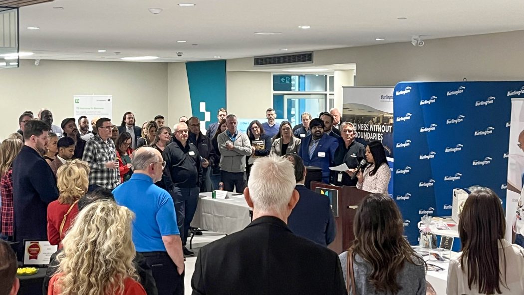 A large group of people listen to a woman speak from a podium.
