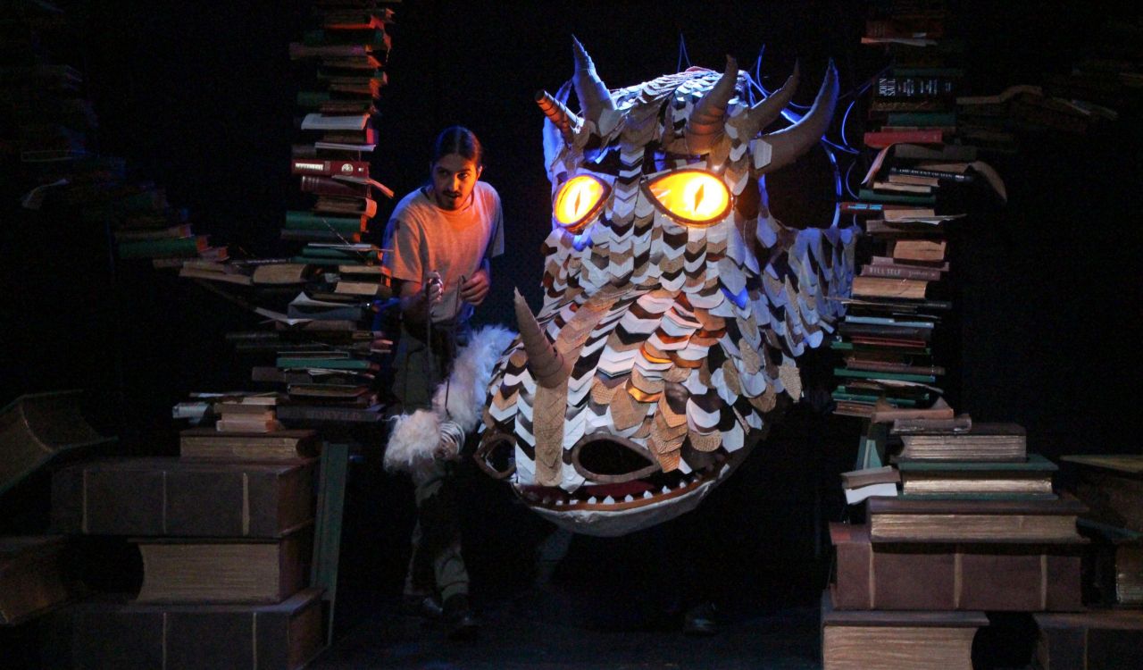 An actor stands on stage beside a large dragon.
