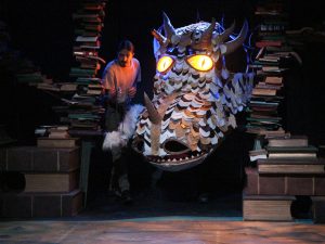 An actor stands on stage beside a large dragon.