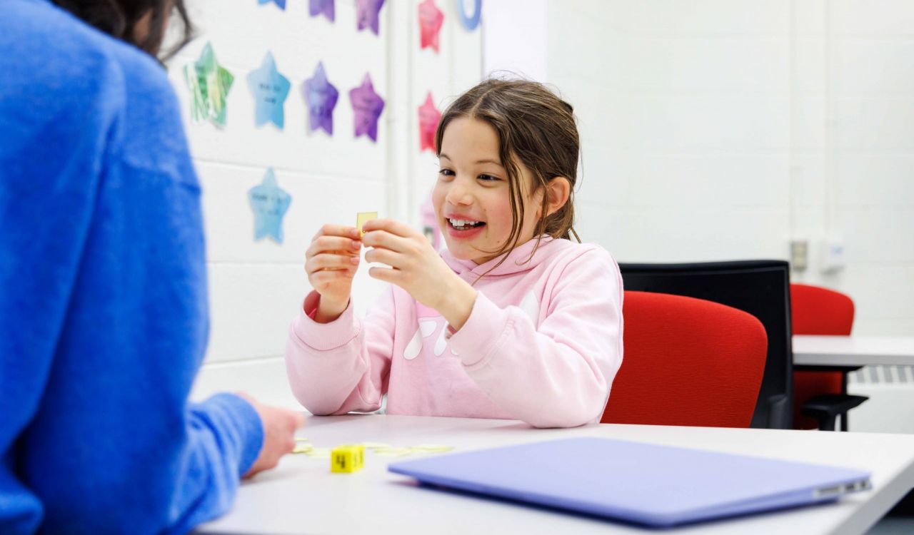 A primary student sits in a learning facility smiling.