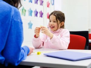 A primary student sits in a learning facility smiling.