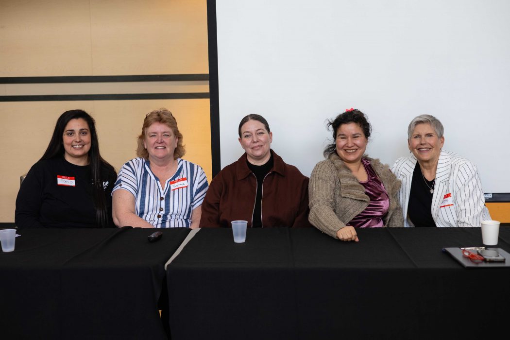 Five people pose for a photo while sitting at a table.
