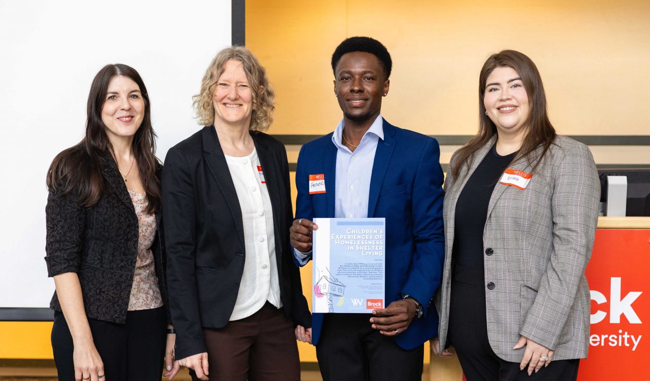 Four people pose with a report in front of a podium and presentation screen.