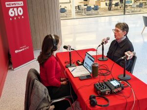 Two people conduct a radio interview, speaking into microphones while seated at a table.
