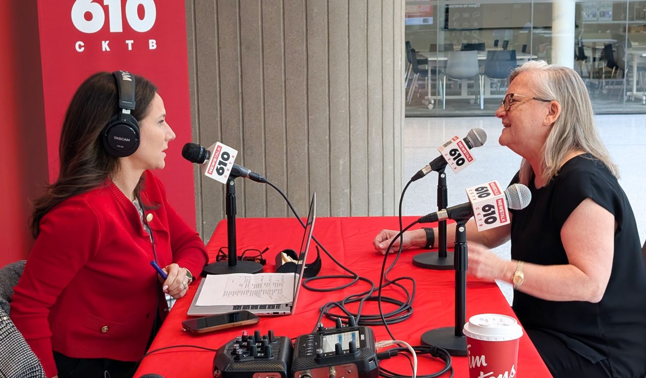 Two people conduct a radio interview, speaking into microphones while seated at a table.