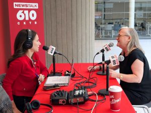 Two people conduct a radio interview, speaking into microphones while seated at a table.