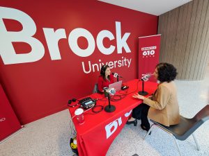 Two people conduct a radio interview, speaking into microphones while seated at a table.