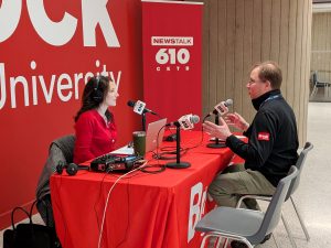 Two people conduct a radio interview, speaking into microphones while seated at a table.