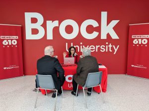 Three people conduct a radio interview while sitting at a table and speaking into microphones.