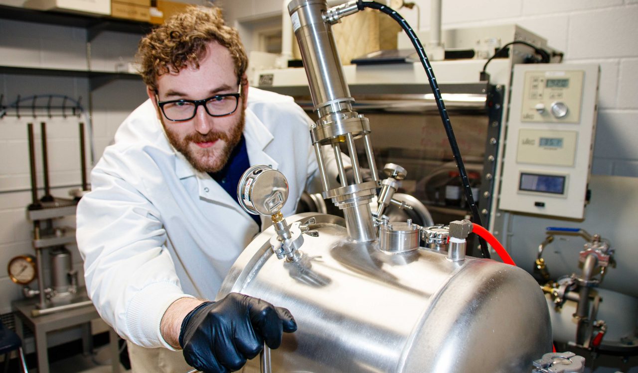 A man in a lab coat works with research equipment.