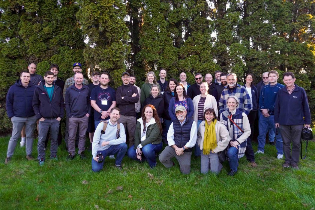 A group of people stand together smiling at a camera outdoors.