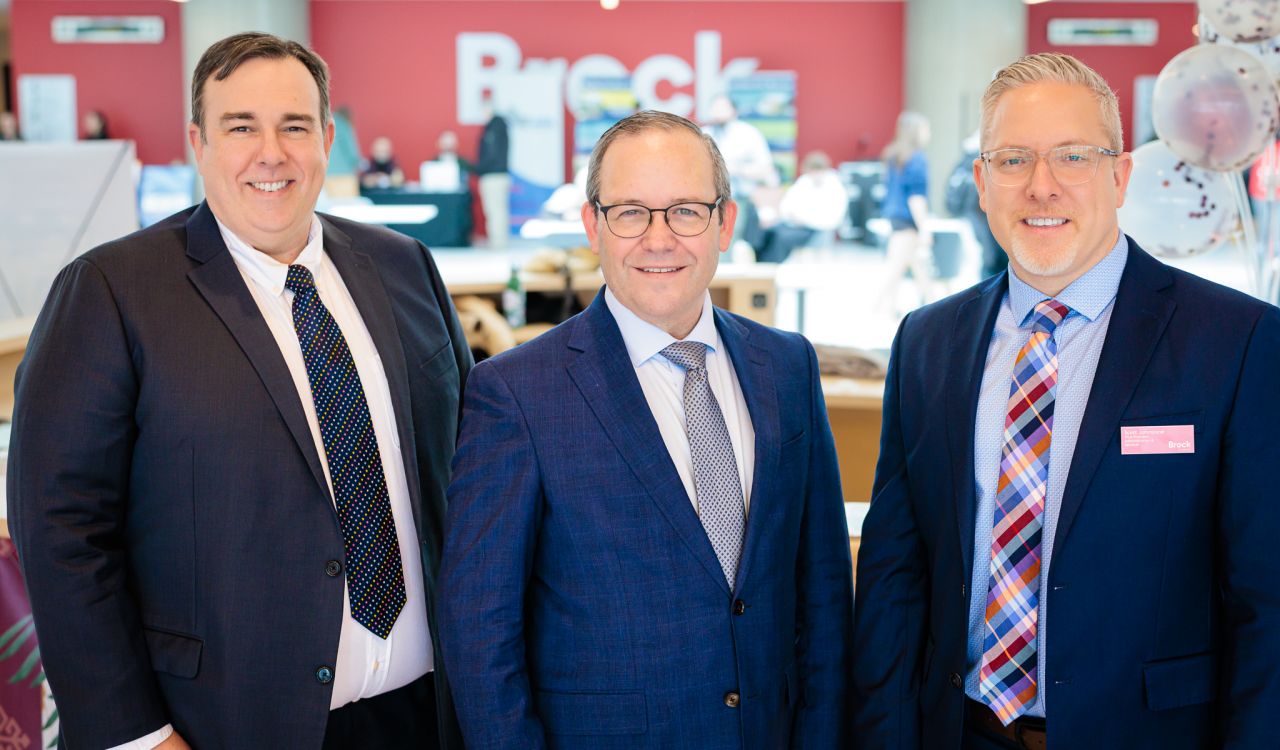 Three men in suits pose for a photo in a brightly lit space.
