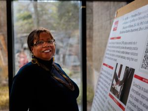 A woman smiles standing beside a large research poster.
