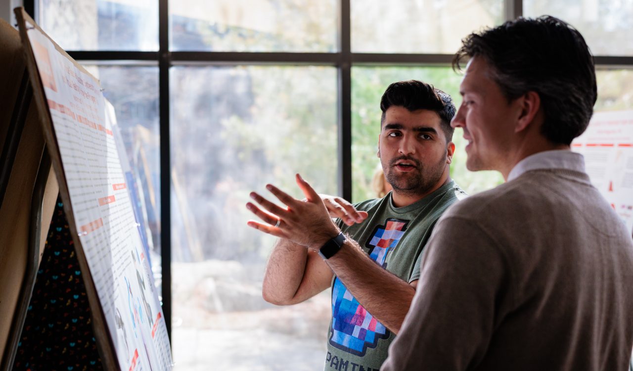 Two people stand together talking and looking at a research poster.
