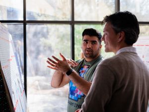 Two people stand together talking and looking at a research poster.