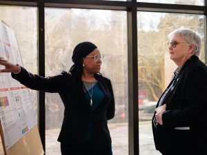 Two people stand together speaking and look at a research poster.