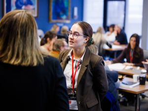 Two people chat at a business event in a room full of people.