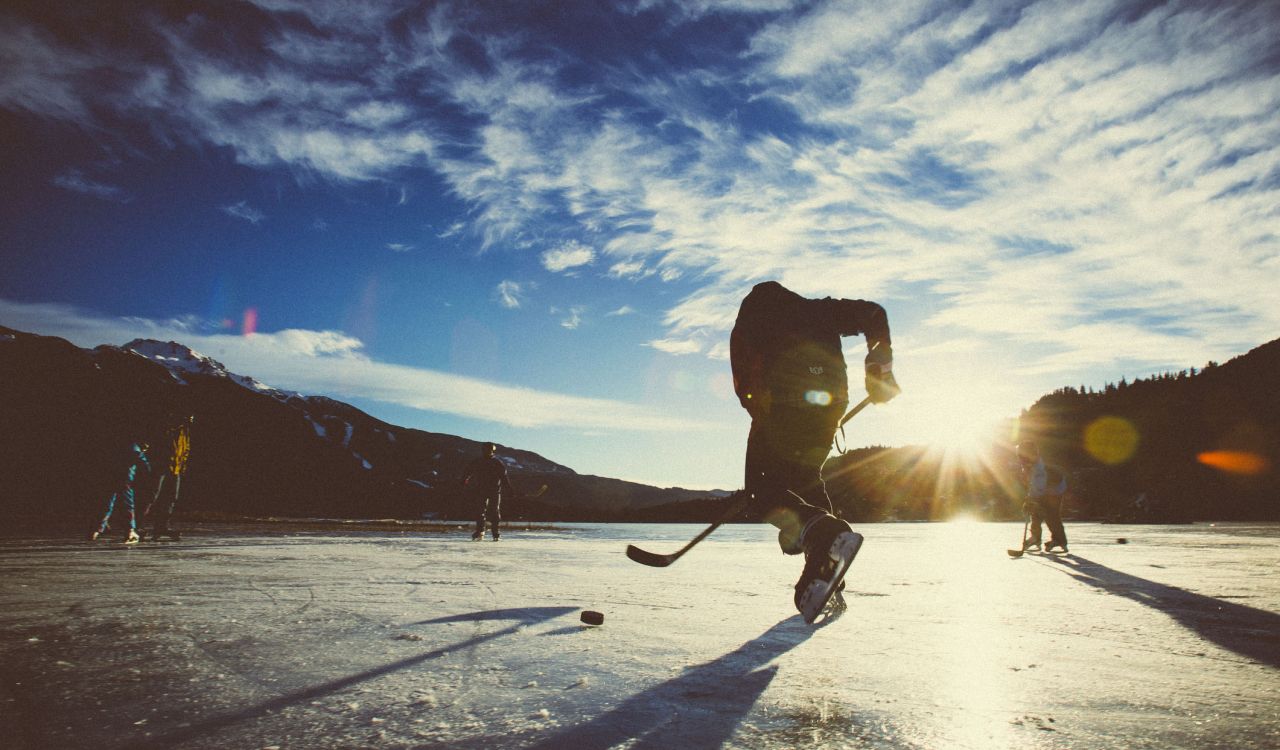 Hockey players on a frozen lake at sunset.