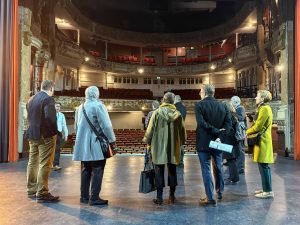 A group of people look out at an empty theatre while standing on a stage.