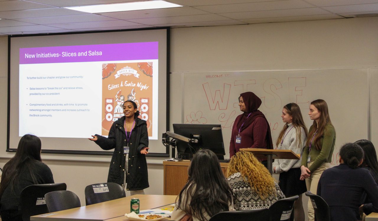 Four young women speak at the front of a room at a university.