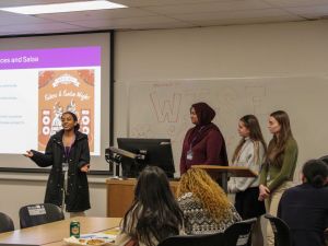Four young women speak at the front of a room at a university.