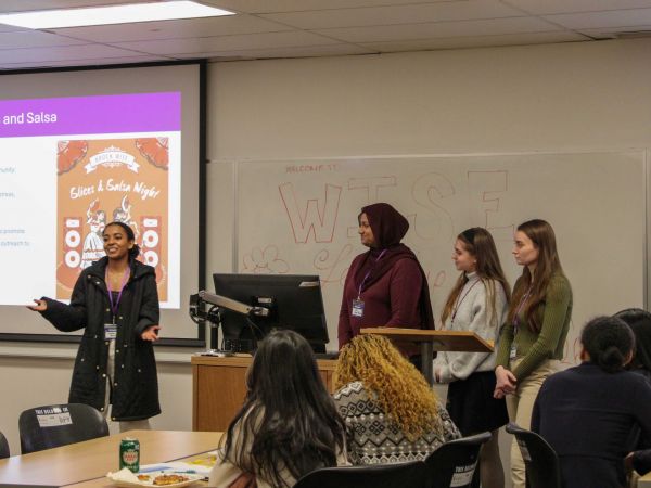 Four young women speak at the front of a room at a university.