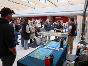 A large group of people walk around an information fair about water.