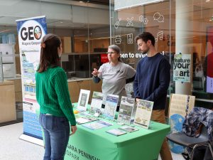 Two people behind a table speak to a community member at a water information fair.