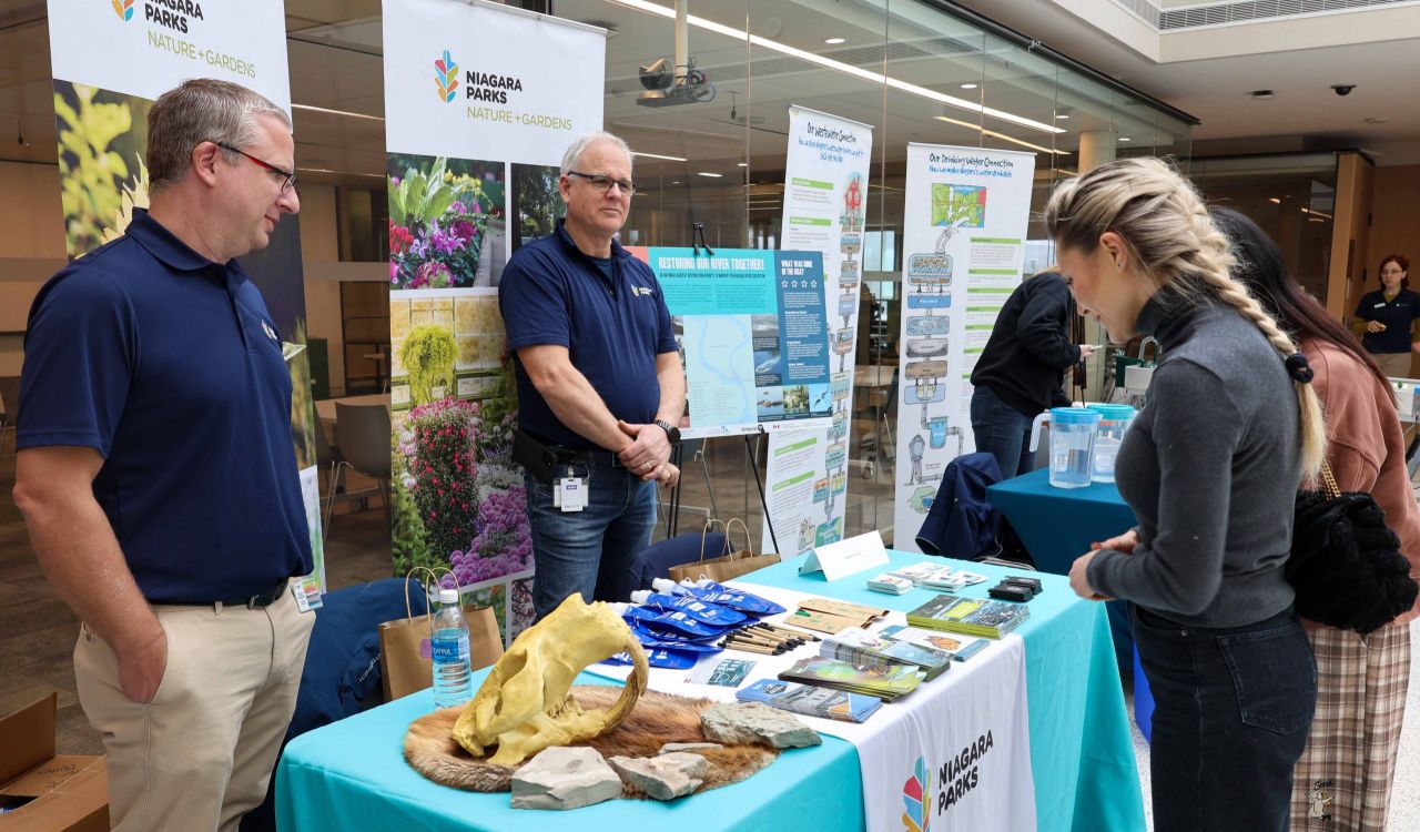 Two people behind a table speak to a community member at a water information fair.