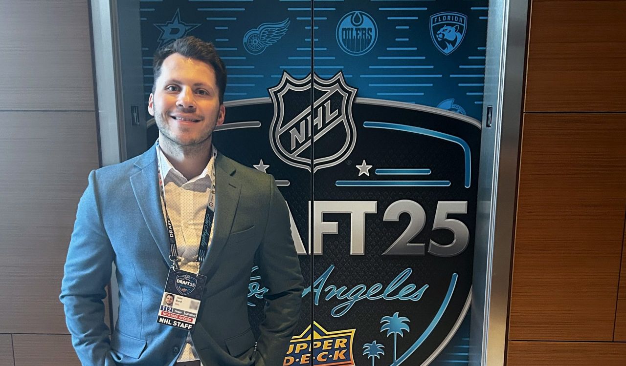 A man in a suit stands in front of a door with the NHL logo on it.